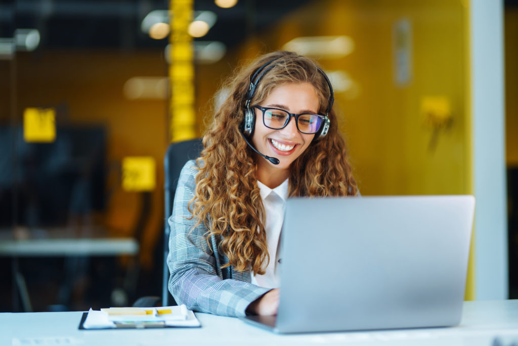 Pay Per Call center agent with headset working on support hotline in modern office.